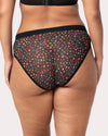 Rear view of a model wearing sheer black mesh bikini bottoms with a dense multicolor floral print, set against a plain light gray background.