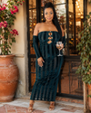 Woman in a dark green strapless dress holding a glass of wine outdoors.