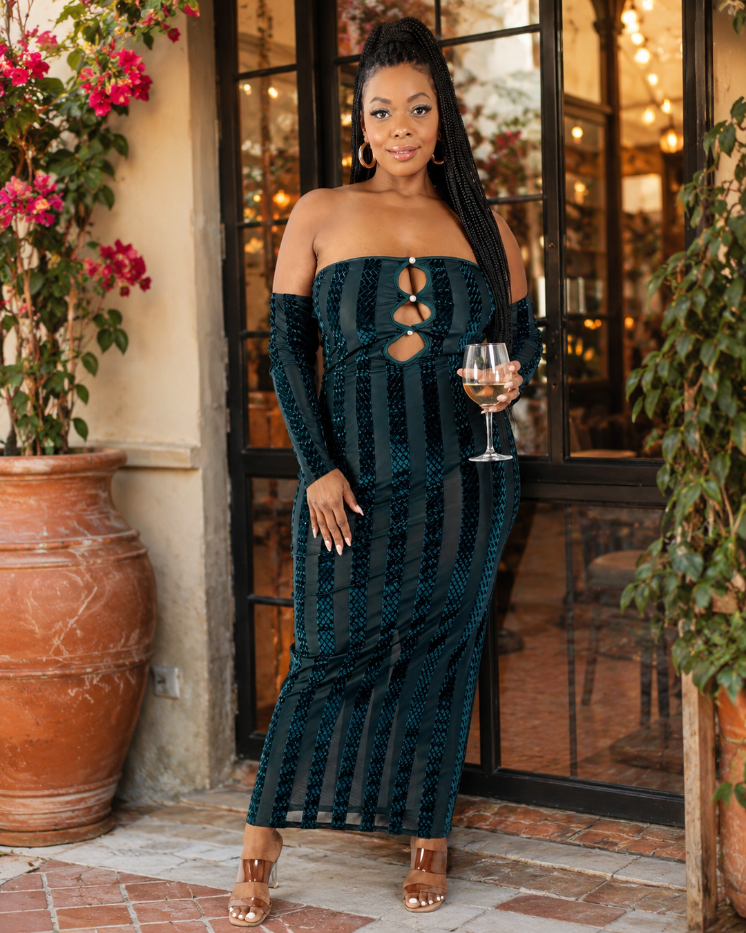 Woman in a dark green strapless dress holding a glass of wine outdoors.