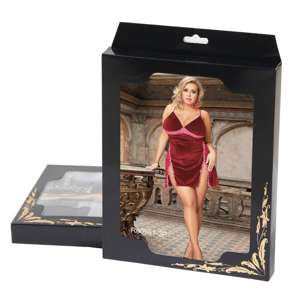A black retail display box with a clear window showing a model wearing a short burgundy velvet dress with pink trim. A second empty display box lies beside it on a plain white background.