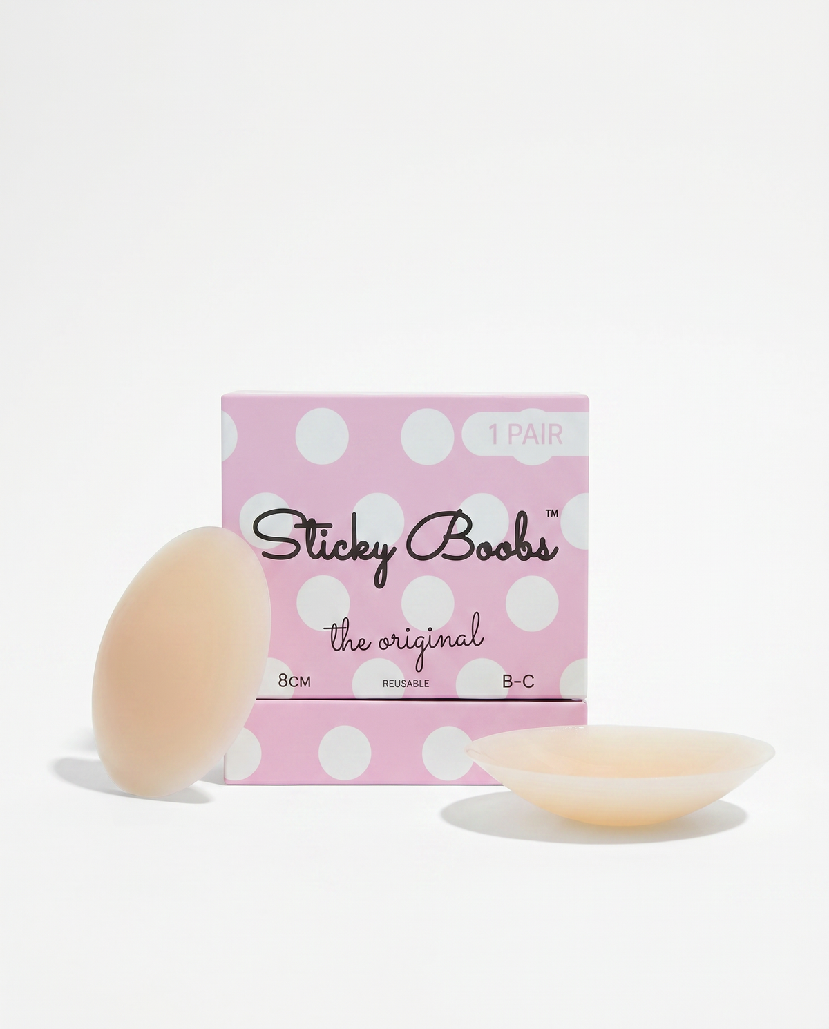 A pink polka-dot box labeled 'Sticky Boobs the original' with two pale peach adhesive pads placed in front on a clean white background.